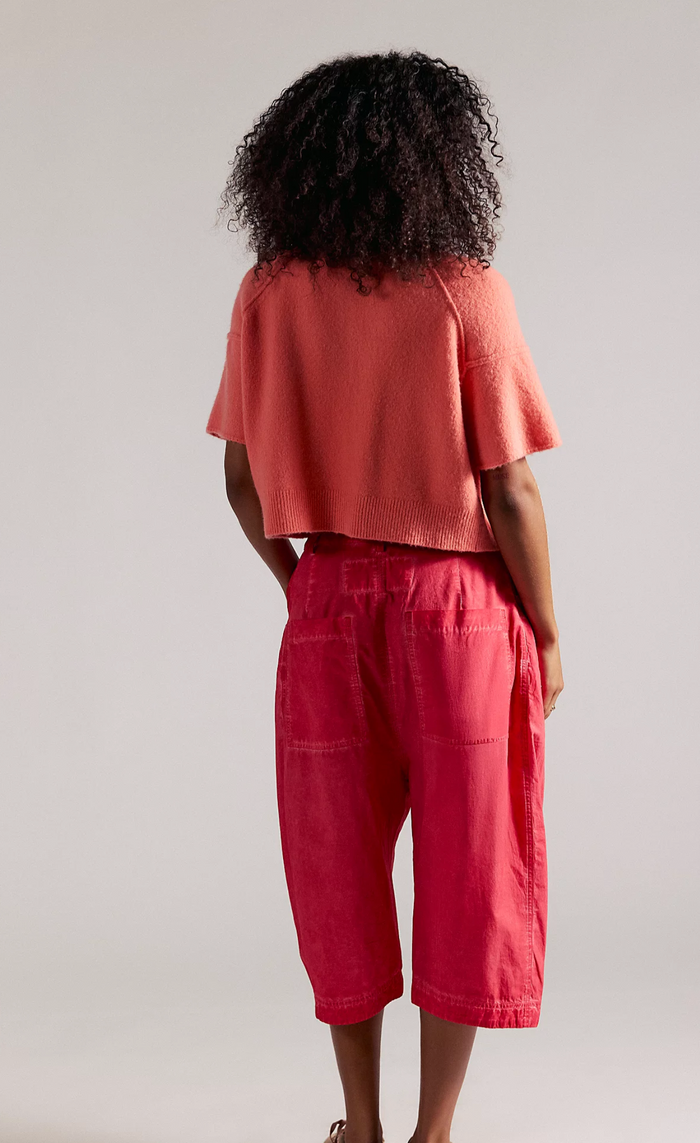 Person wearing a coral top and red pants against a plain background