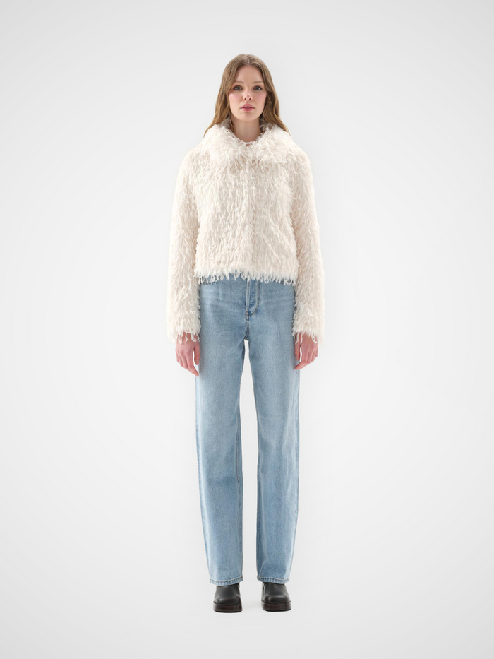 White faux fur jacket with high funnel neck and cropped fit, long pile, feather texture, worn over light-wash straight-leg jeans, front view