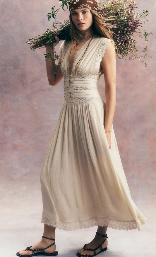 Woman in a flowing dress holding flowers against a plain background