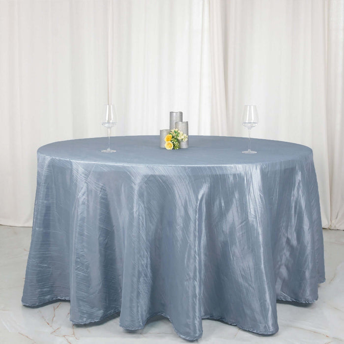 Round table dressed in a silver tablecloth with decorative centerpieces and glassware.