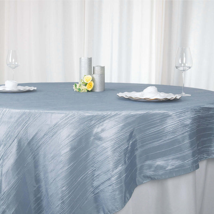 Elegant silver tablecloth draped over round table with glassware and candles.
