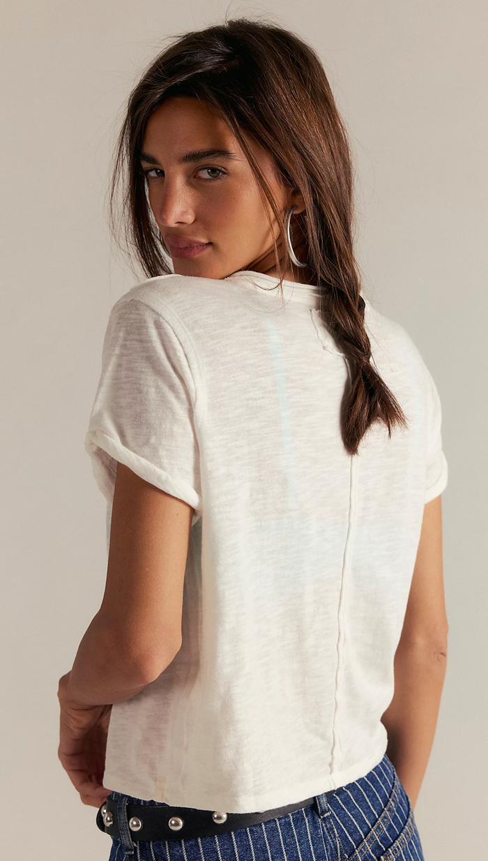Woman wearing a ivory t-shirt and blue jeans against a plain background
