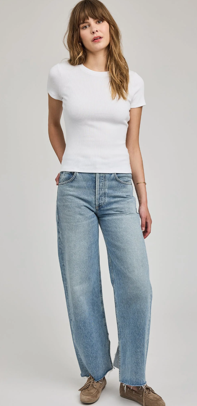 Woman wearing a white t-shirt and light blue jeans on a plain background