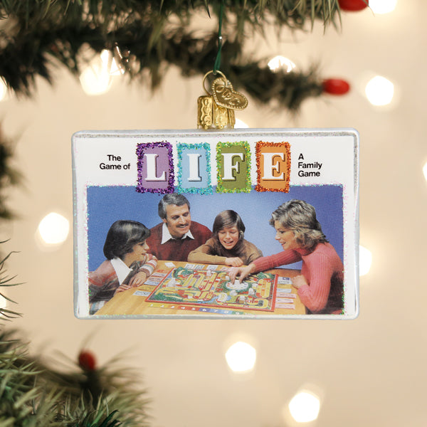 A Christmas tree ornament featuring an image of a family of four playing The Game of Life board game, with â€œLIFEâ€_x009d_ spelled out in colorful glittery letters above them.