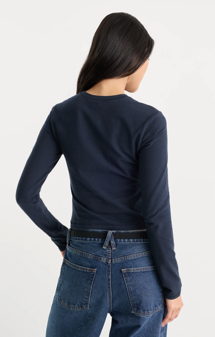 A woman shown from the back wearing a dark navy long-sleeve crewneck top and blue jeans against a plain white studio background.