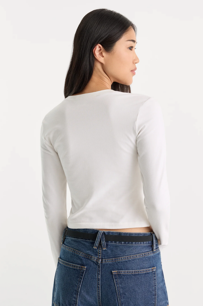 A woman shown from the back wearing a fitted white long-sleeve top and blue jeans against a plain light background.