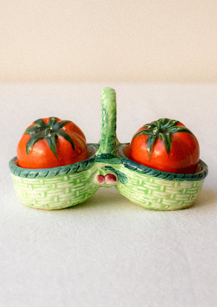 Salt and pepper shakers shaped like tomatoes in a decorative green basket.
