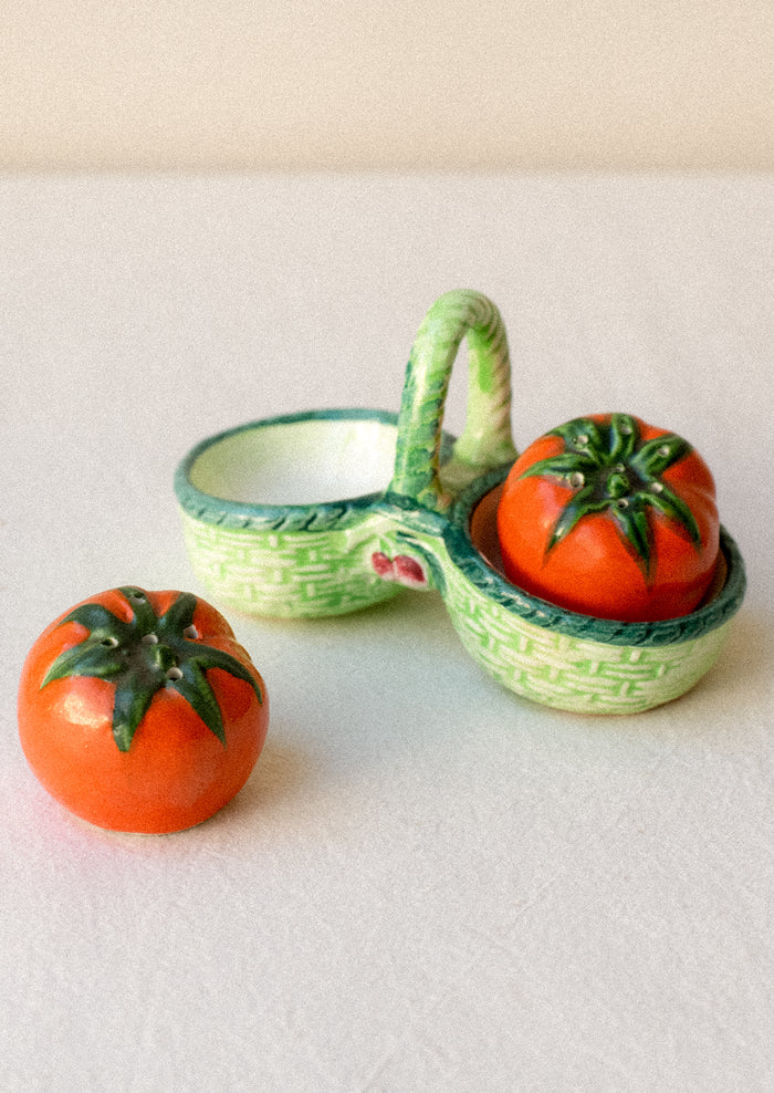 Salt and pepper shakers shaped like tomatoes in a decorative green basket.