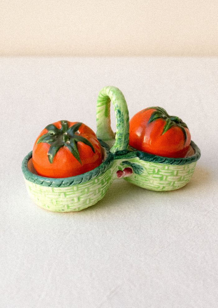 Salt and pepper shakers shaped like tomatoes in a decorative green basket.