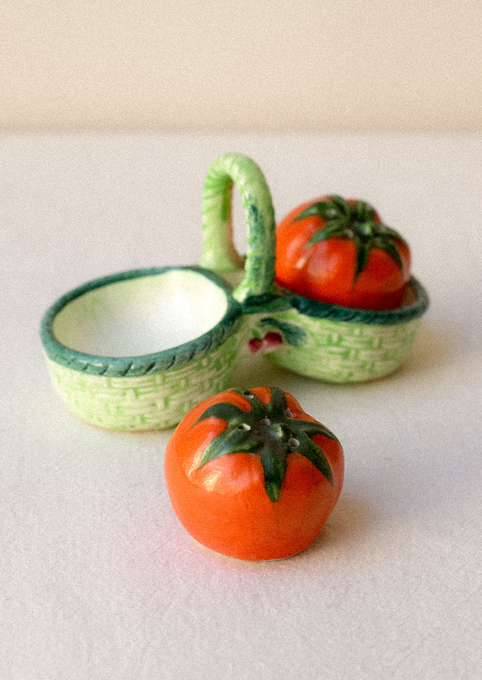 Salt and pepper shakers shaped like tomatoes in a decorative green basket.