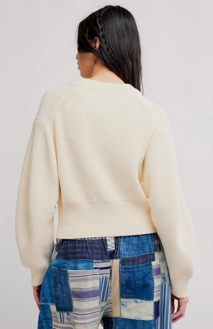 Person wearing a cream sweater and patterned pants on a plain background