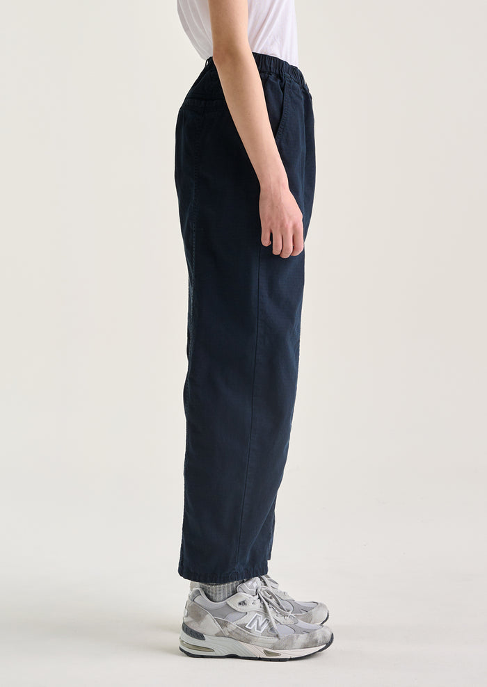 A woman wearing a pair of navy blue pants with tapered leg, in ripstop cotton fabric.