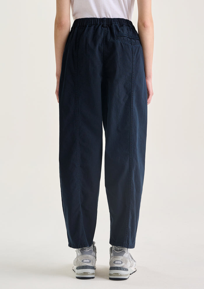 A woman wearing a pair of navy blue pants with tapered leg, in ripstop cotton fabric.