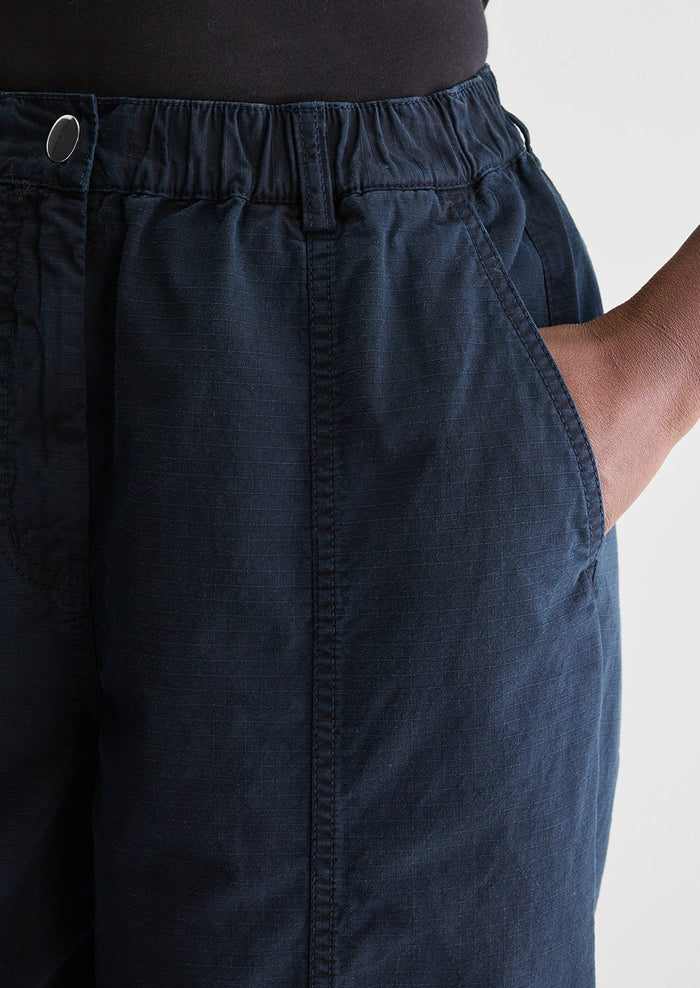 A woman wearing a pair of navy blue pants with tapered leg, in ripstop cotton fabric.