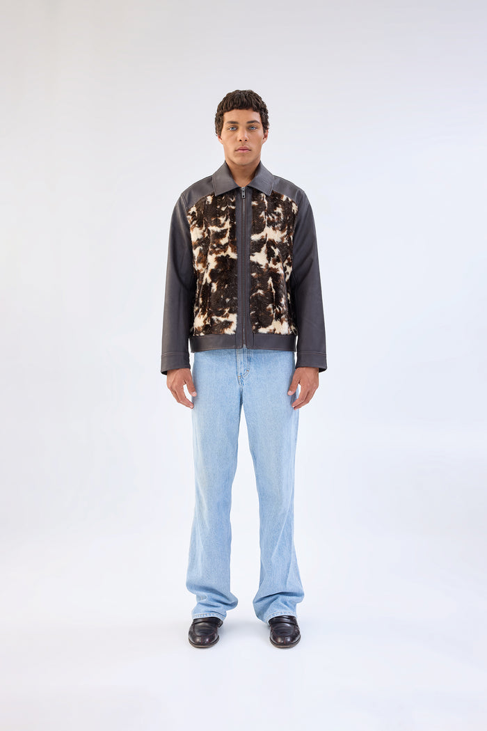 Brown faux leather jacket with cow-print faux fur front panel, point collar and zip-front closure, worn over light-wash straight-leg jeans, front view