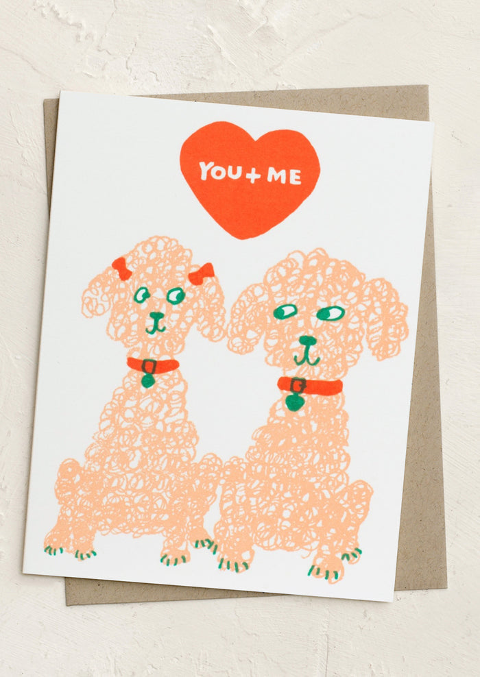 A card with sketch of two poodles, red heart and top with text reading "You + me".